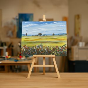 Pintura al óleo de un paisaje campestre con flores de colores en primer plano, un prado verde y árboles bajo un cielo azul con nubes.